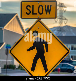 Square Pedestrian crossing road sign against houses vehicles mountain and cloudy sky Stock Photo