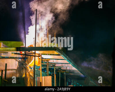 SINGAPORE - 9 JUNE 2019 - Construction worker in performs metal welding work at a building site for at night, creating a vertical plume of smoke. With Stock Photo