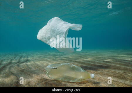 Plastic ocean pollution underwater, a plastic bag adrift and a bottle on a sandy bottom Stock Photo