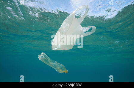 Underwater pollution, a plastic bag and a bottle adrift below water surface in the sea Stock Photo