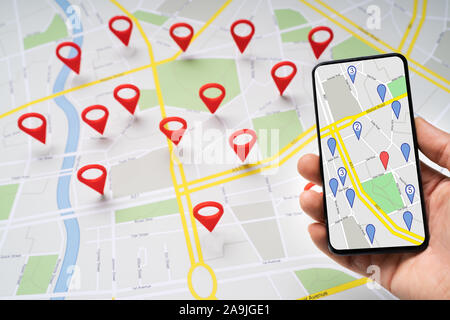Person's Hand Holding Mobile Phone Against Road Map With Red Navigation Icons Stock Photo