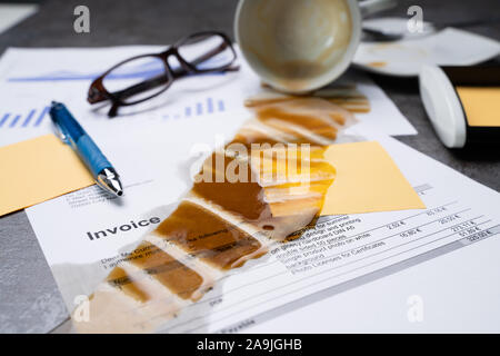 Close-up Of Coffee Spilling Out From Cup Over Graph And Invoice On Office Desk Stock Photo