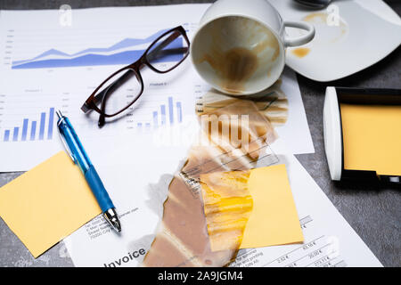 Close-up Of Coffee Spilling Out From Cup Over Graph And Invoice On Office Desk Stock Photo