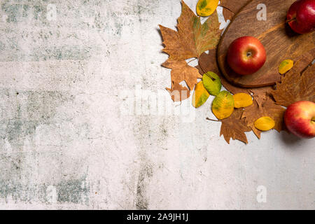 Autumn cozy composition. Red apples on the wooden board. Autumn leaves, on  gray concrete background. Flat lay. Stock Photo