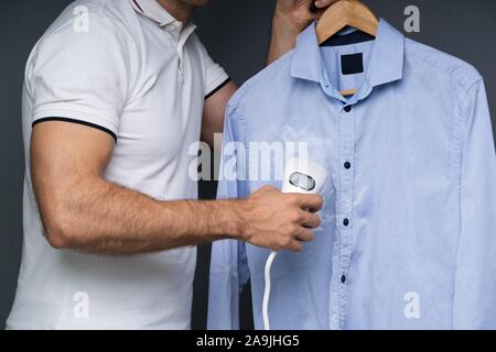 Close-up Of A Man Steaming Blue Shirt Using Electric Steamer Stock Photo