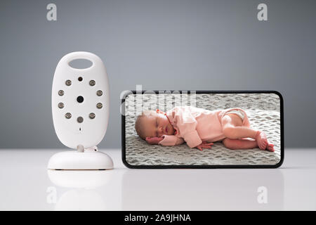 Close-up Of Wireless Camera And Smartphone With Baby Image On Screen On Reflective Table Stock Photo