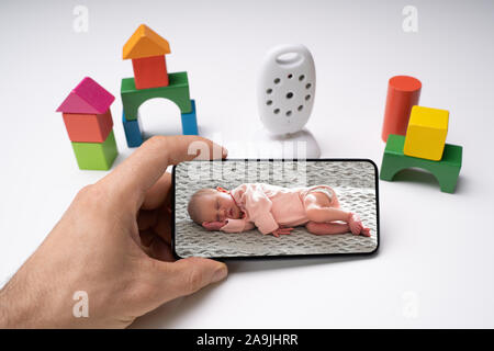 Person's Hand Holding Mobile Phone With Baby Image Near Wireless Camera Stock Photo