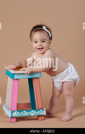 One little baby girl standing with kids chair on studio background