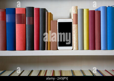 Mobile phone in bookshelf with sorted books Stock Photo
