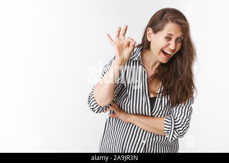 Feeling totally okay. Portrait of healthy and active elderly woman with long hair and wrinkles bending towards camera, grimacing funny, winking cheeky Stock Photo