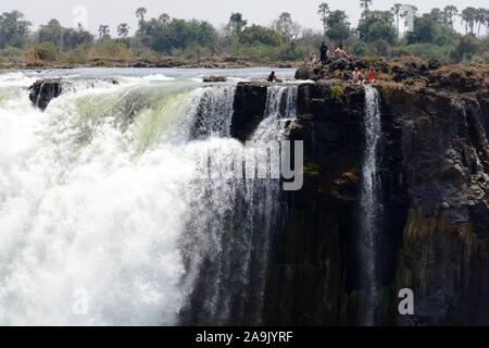 People tourists swimming in Devils Pool  on the edge of Victoria Falls Livingstone Island Zambia taken from the Zimbabwe side Africa Stock Photo