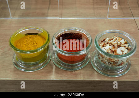 glass jars on a wooden shelf containing ground spices of different colors Stock Photo