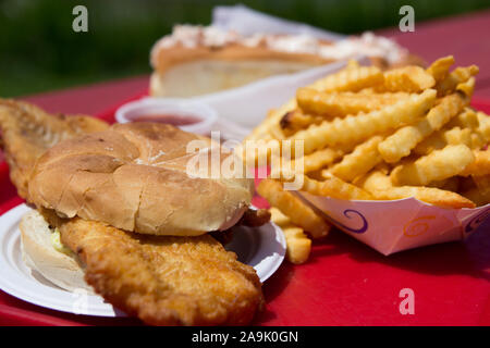 Closeup food product shot of a fried fish sandwich on a bun, french fries and a lobster roll, served on a red plastic tray outdoors. In Maine, United