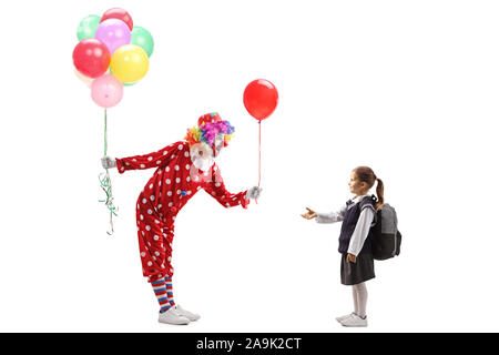 Full length profile shot of a clown holding a bunch of balloons and giving one to a little schoolgirl isolated on white background Stock Photo