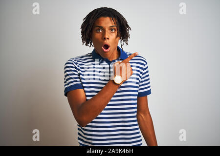 Afro man with dreadlocks wearing striped blue polo standing over isolated white background Surprised pointing with finger to the side, open mouth amaz Stock Photo