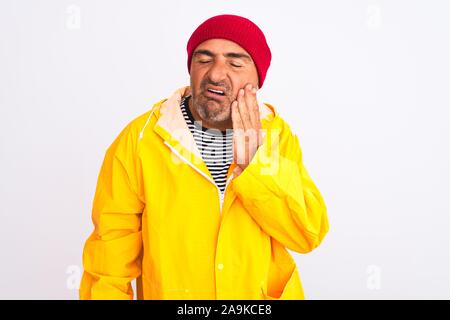 Middle age man wearing rain coat and woolen hat standing over isolated white background touching mouth with hand with painful expression because of to Stock Photo