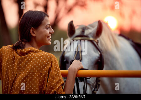 Pretty smiling woman  and her horse in the sunset, horse ranch concept Stock Photo