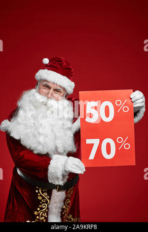 Senior man wearing Santa costume making a big sale and holding sale signs in his hands isolated on red background Stock Photo