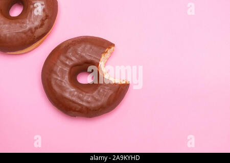 Two chocolate frosting donuts with one donut bitten on soft pink background Stock Photo