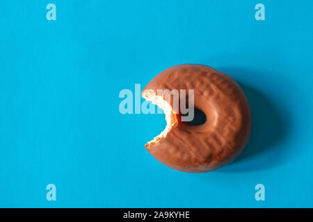 Tasty bitten doughnut with chocolate frosting on bright blue background Stock Photo