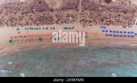 Aerial view of green, red, blue umbrellas and reclining sunbeds on a sandy beach by shallow sea waters . Stock Photo