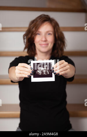 Pregnant woman feeling happy at home while taking care of her child. The young expecting mother holding baby in pregnant belly. Maternity prenatal car Stock Photo