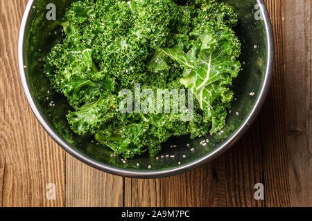 Ingredients for kale chips: Kale mixed with olive oil, salt, sesame and lemon juice in metal bowl on textured wooden surface  - top down view Stock Photo