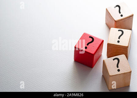 Individuality, diversity and leadership concept with three natural wood cubes and one red cube printed with question marks on a white background with Stock Photo