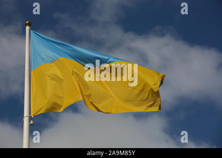 Flag of Ukraine waves on white flagpole against blue sky with white nice clouds Stock Photo