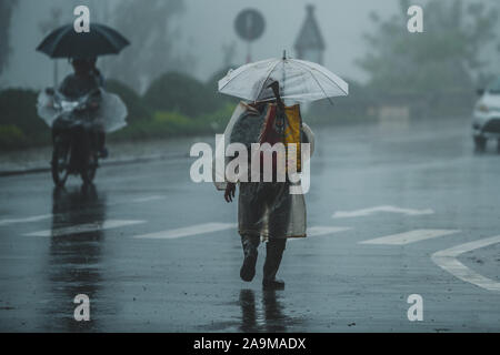 Sapa, Vietnam - 13th October 2019: An old Asian man under an umbrella walks away from the camera in the pouring rain in the small town of Sapa Stock Photo