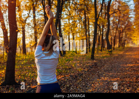Training and exercising in autumn park. Woman stretching arms outdoors. Active healthy lifestyle Stock Photo