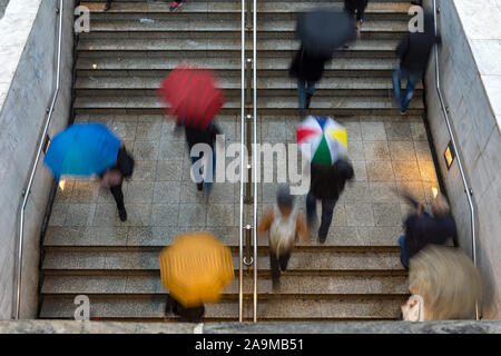 overhead view of people walking towards and away from the entrance to the underground train station under rain with umbrellas - bad weather Stock Photo