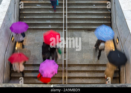 overhead view of people walking towards and away from the entrance to the underground train station under rain with umbrellas - bad weather Stock Photo