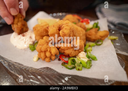 Crispy salt and pepper breaded squid with a lemon mayonnaise dip plus chilli, spring onion and corriander salad on a glass plate. A man is dipping one Stock Photo