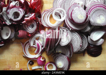 Red Onions sliced with skins on the side on a wooden cutting board Stock Photo