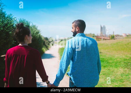 Young couple in casual wear walking away with hand in hand at sunset Stock Photo