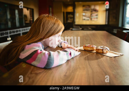 Young Red Haired Girl Looking Longingly at Delicious Doughnuts Stock Photo