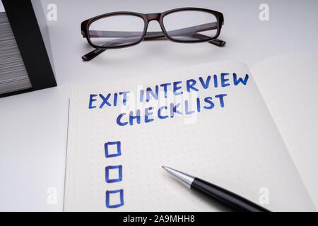 Handwritten Exit Interview Checklist Message On Notebook With Blue Marker And Spectacles Over Office Desk Stock Photo