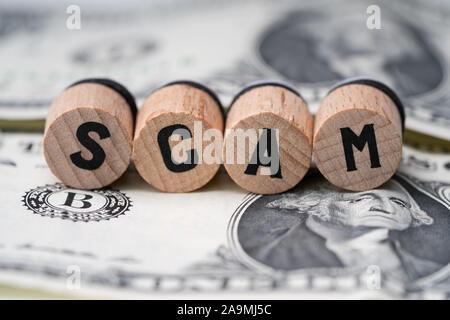 Close-up Of A Scam Word On Round Wooden Blocks Over Dollar Bill Stock Photo