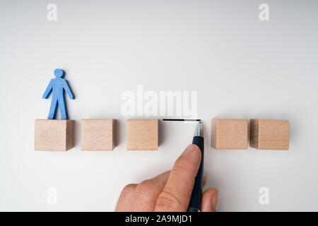 Human Hand Filling Gap Between Wooden Blocks Arranged In A Row With Blue Human Figure Stock Photo