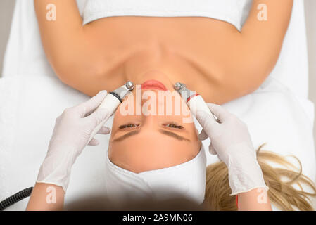 woman close up receiving electric facial massage on microdermabrasion equipment at beauty salon. rf lifting procedure in a beauty parlour. Top view Stock Photo