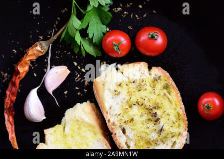 In a dark pan are two slices of white bread and olive oil, surrounded by peppers, tomatoes, garlic and parsley with oregano Stock Photo