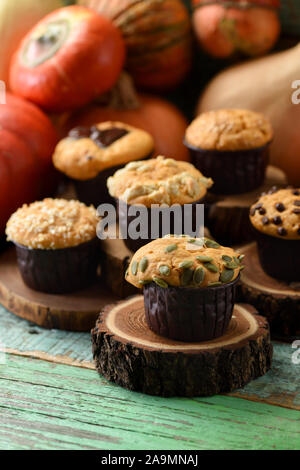 Homemade healthy pastry concept. Yummy imperfect pumpkin muffins with seeds and chocolate with winter squashes on wood slabs on shabby green backgroun Stock Photo