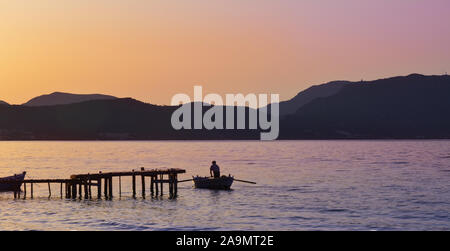 Golden sunset colors with a fisherman rowing near a jetty Stock Photo