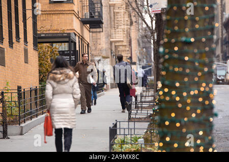 NEW YORK CITY - DECEMBER 14, 2018: New York City street scene at Christmas time with UPS driver delivering Amazon package, pedestrians and lights on t Stock Photo