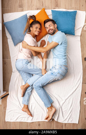 Young adult woman and man lying on bed together and smiling wide Stock Photo