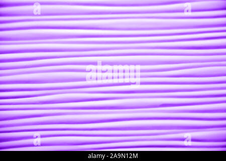 Close-up of artificial textured surface with simple wave pattern toned in shades of purple color. Plenty of smooth horizontal wavy lines. Empty abstra Stock Photo
