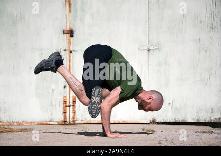 Middle aged man with a beard practicing yoga by an old paint peeling wall. Stock Photo