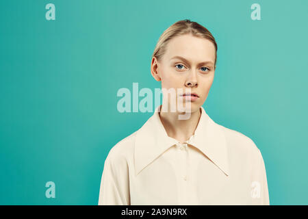 Waist up portrait of young contemporary woman looking at camera with serious face expression while posing against mint blue background, copy space Stock Photo