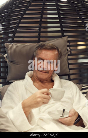 Portrait of wealthy senior man relaxing in lounge chair at luxury SPA resort and drinking coffee Stock Photo